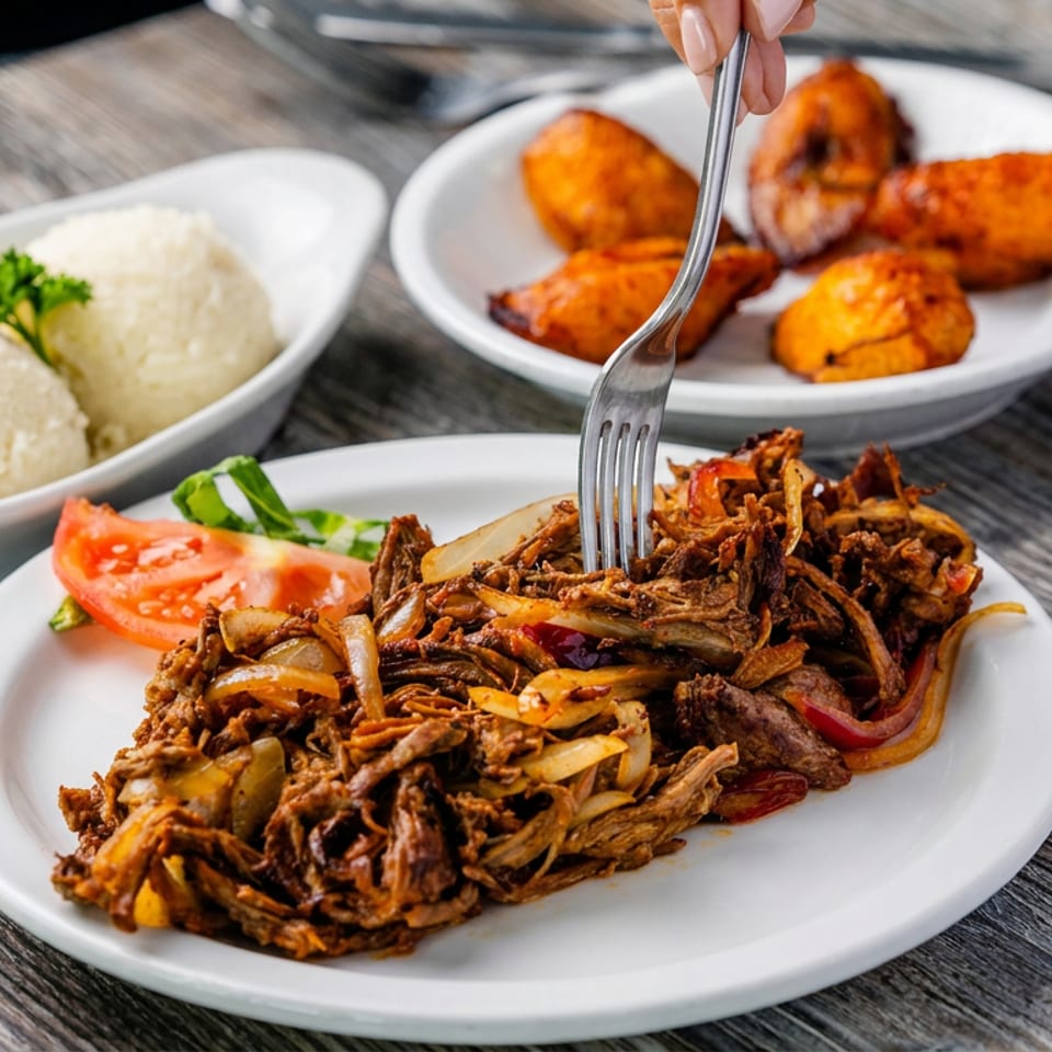 Plated shredded meat sautéed with onions and peppers, served with white rice, tomato garnish, and fried orange appetizers.