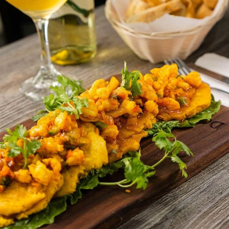 Golden fried plantains topped with spiced shrimp and garnished with cilantro on a lettuce-lined wooden serving board.